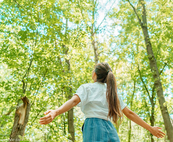 Stimmungsbild einer Frau mit ausgebreiteten Armen im Wald